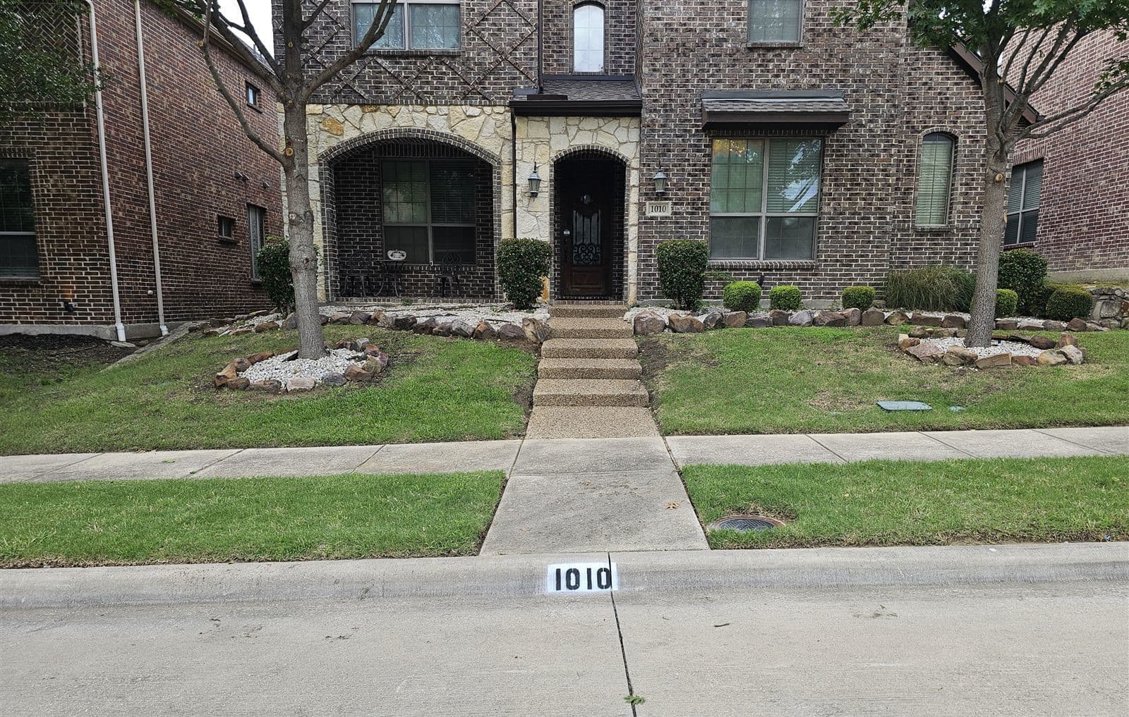 Freshly painted curb address 1010 in crisp black numbers on a bright white background in front of a brick home